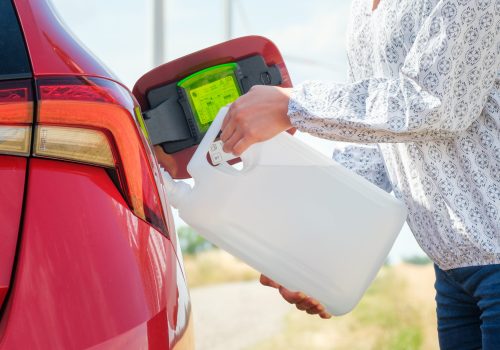 Close up woman refilling the red car with fuel or a diesel engine fluid from canister in the field